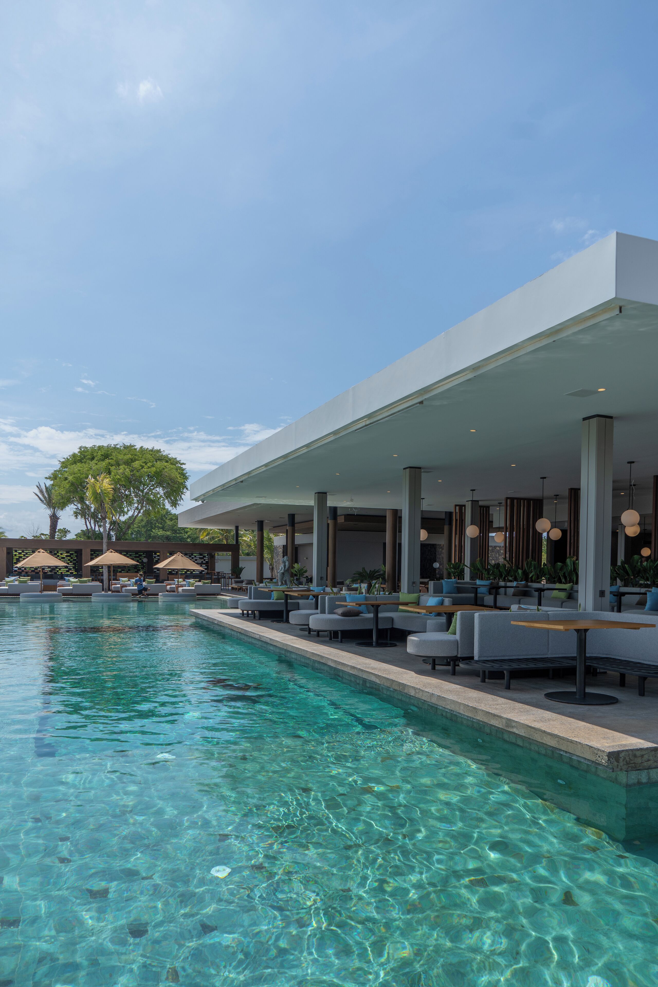 Un área de piscina exterior moderna con agua cristalina, sillas de descanso y sombrillas.