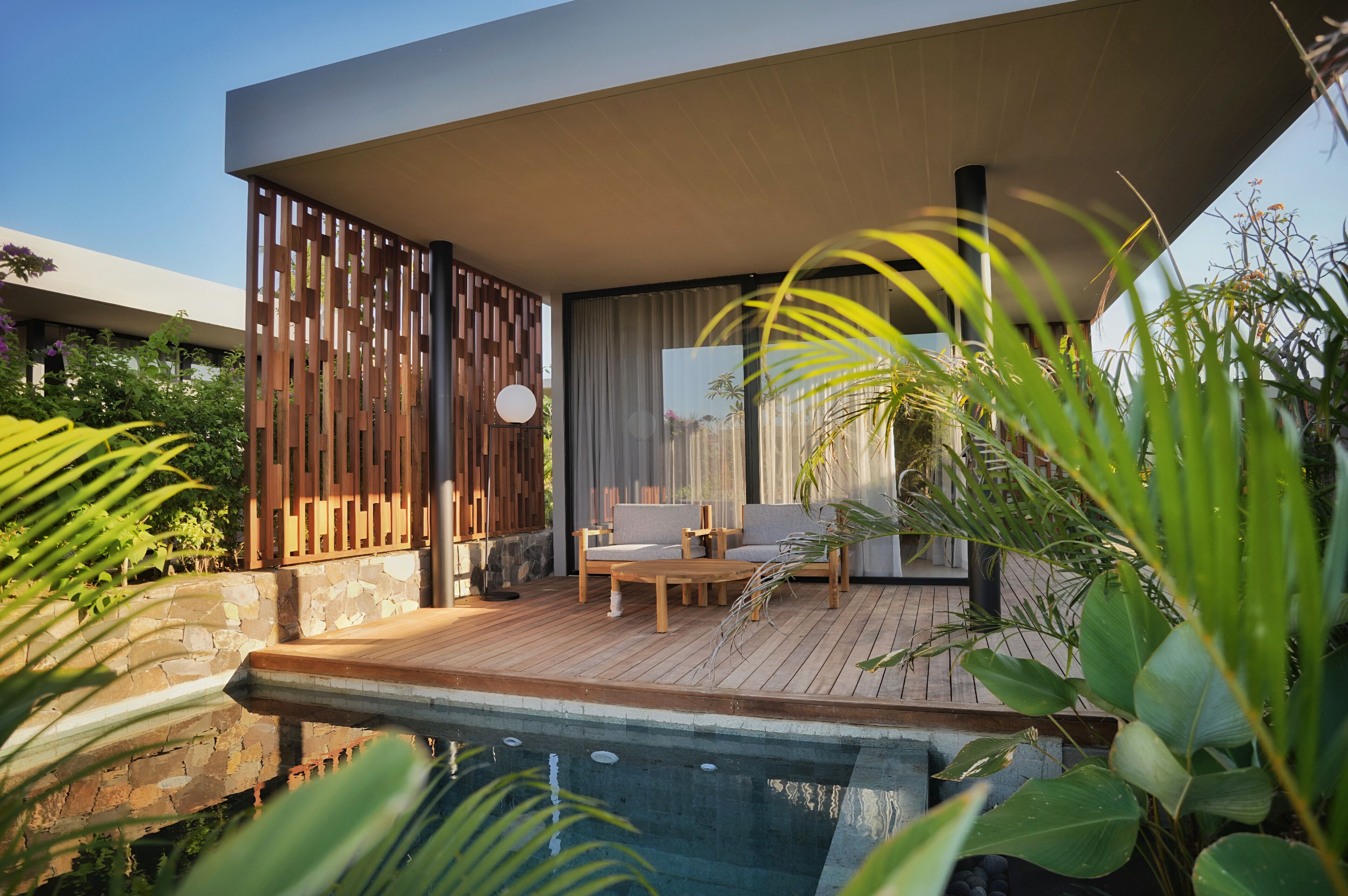 A modern outdoor seating area with a pool, wooden deck, and lush greenery.