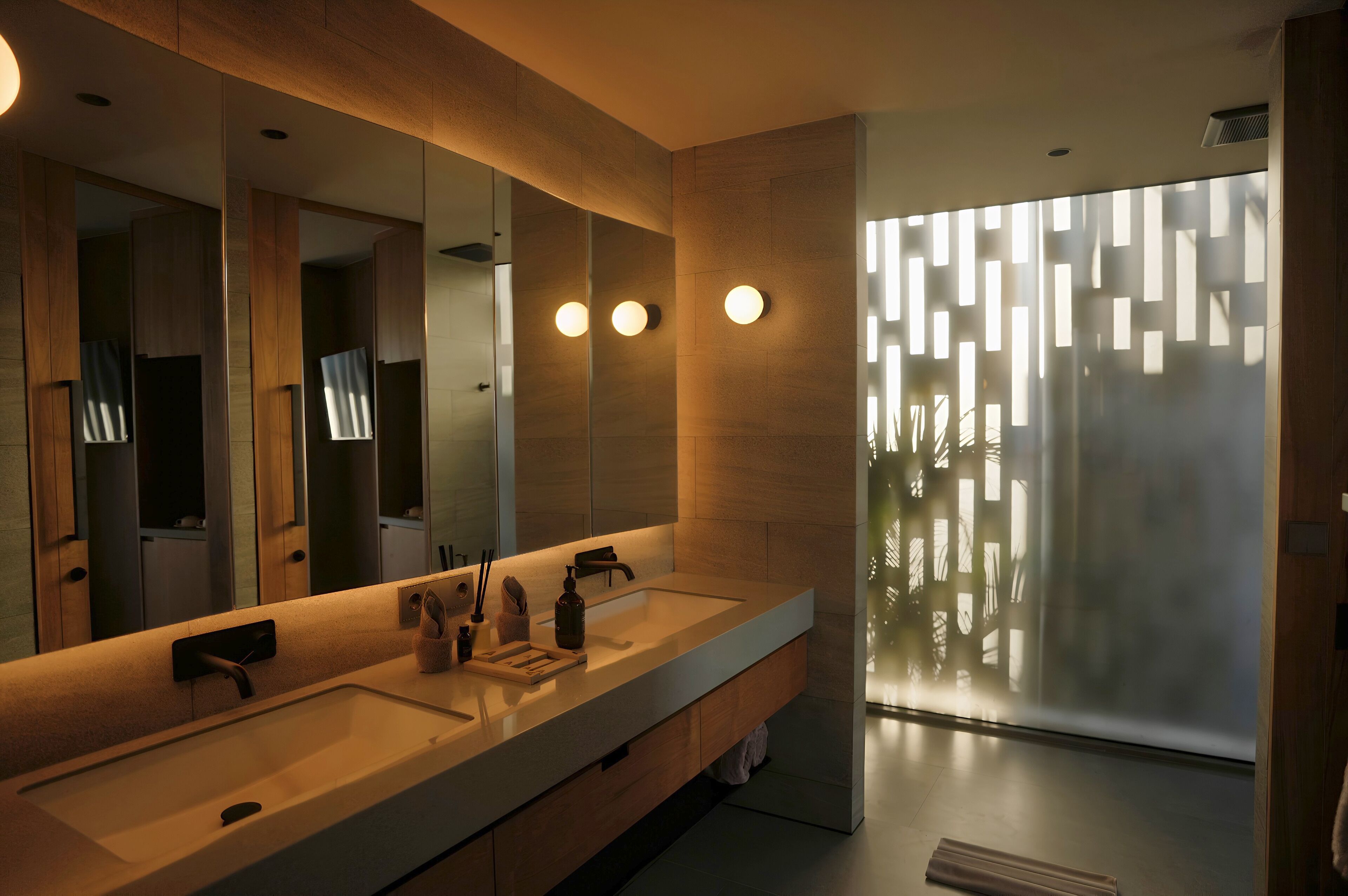 A modern bathroom with a double sink, large mirror, and a frosted glass partition.