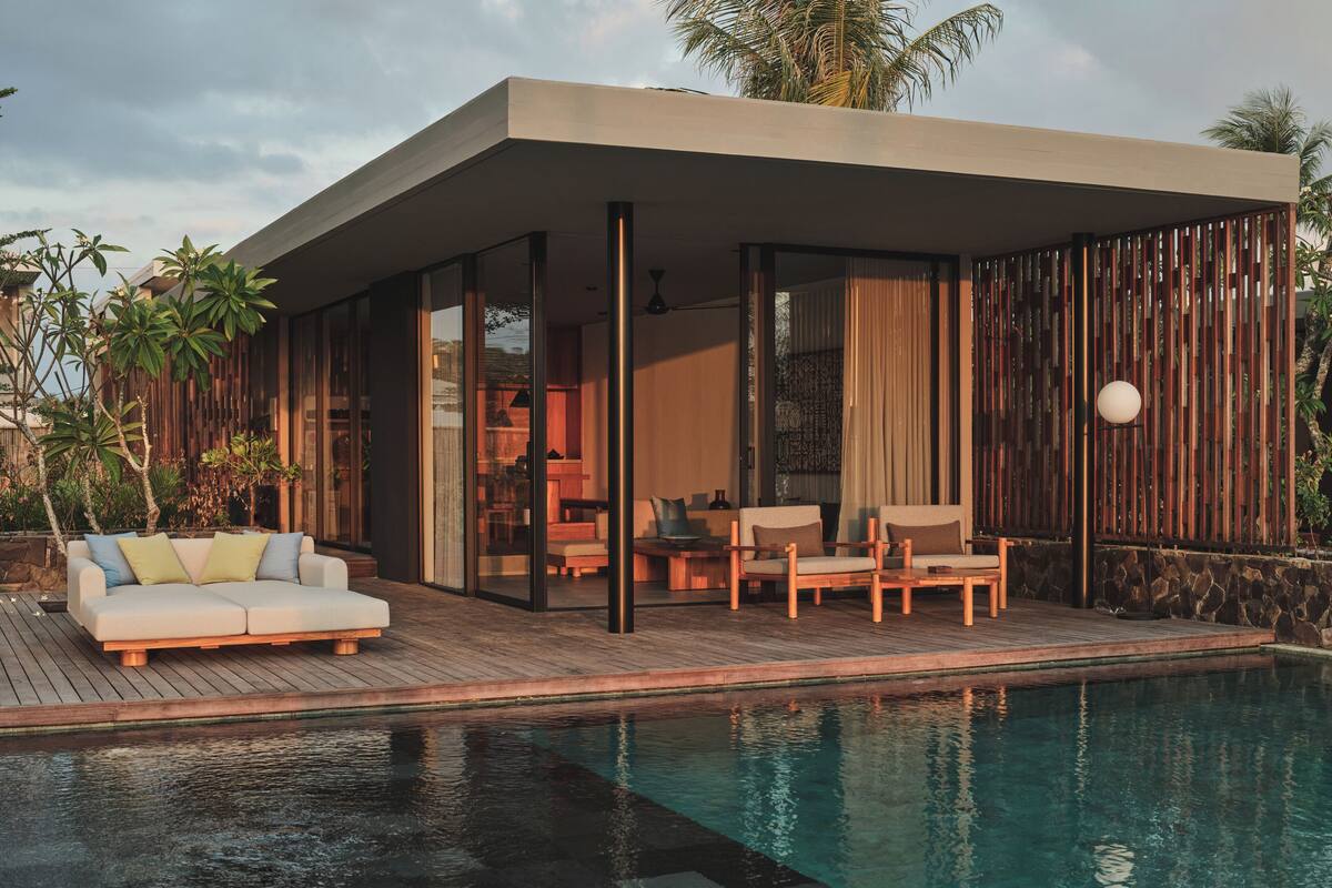 A modern outdoor pool area with a covered seating area, a sofa, and a table.