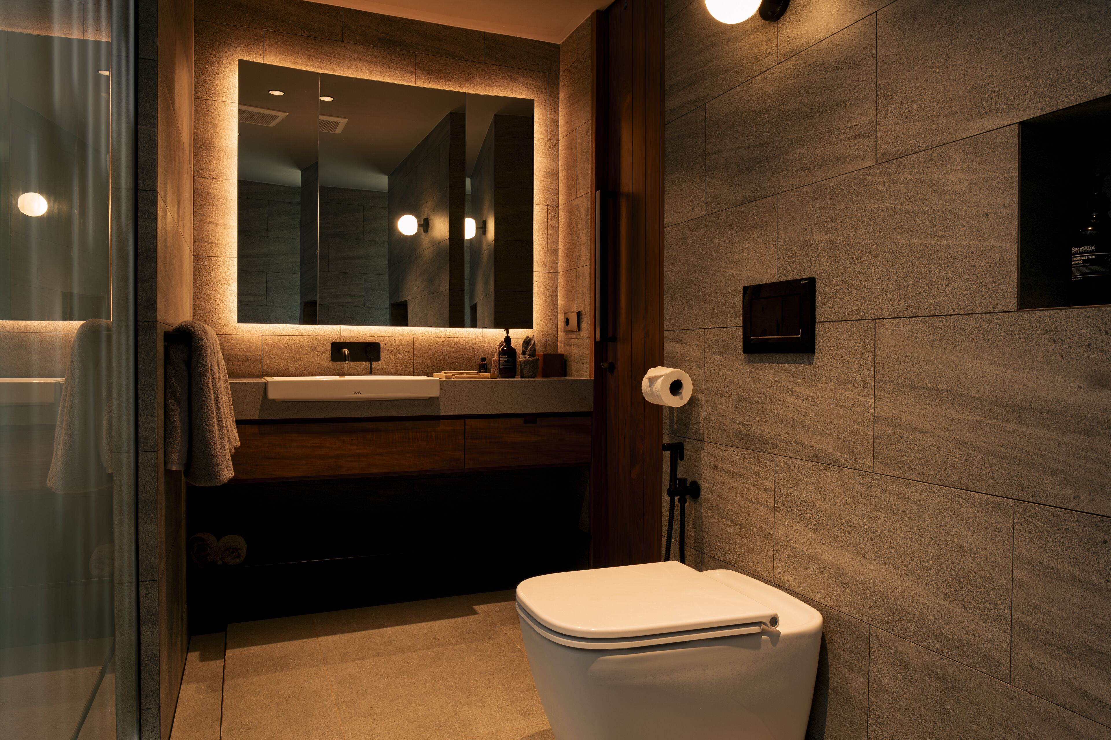 A modern bathroom with a glass shower enclosure, a white toilet, and a wooden vanity with a mirror.