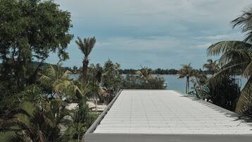 Terraza en la azotea con vistas a un cuerpo de agua tranquilo, rodeada de palmeras y otra vegetación.