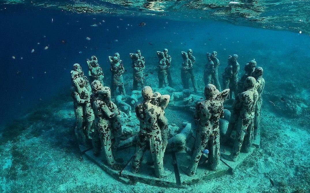 A submerged stone structure with multiple statues, surrounded by marine life.