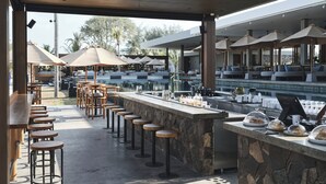Un área de bar al aire libre con diversas opciones de asientos, una barra de piedra y sombrillas que dan sombra.