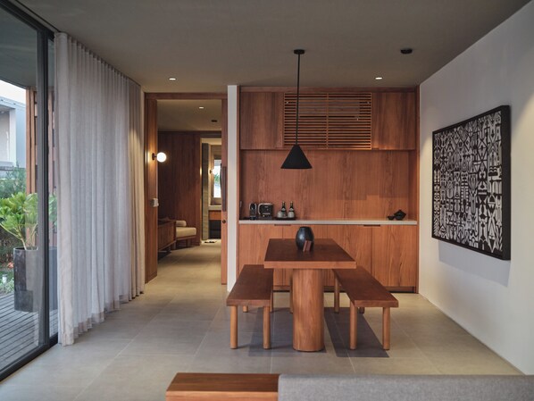 A modern kitchen with wooden cabinets, a dining table with benches, and a pendant light. - BASK GILI MENO (Gili Meno)