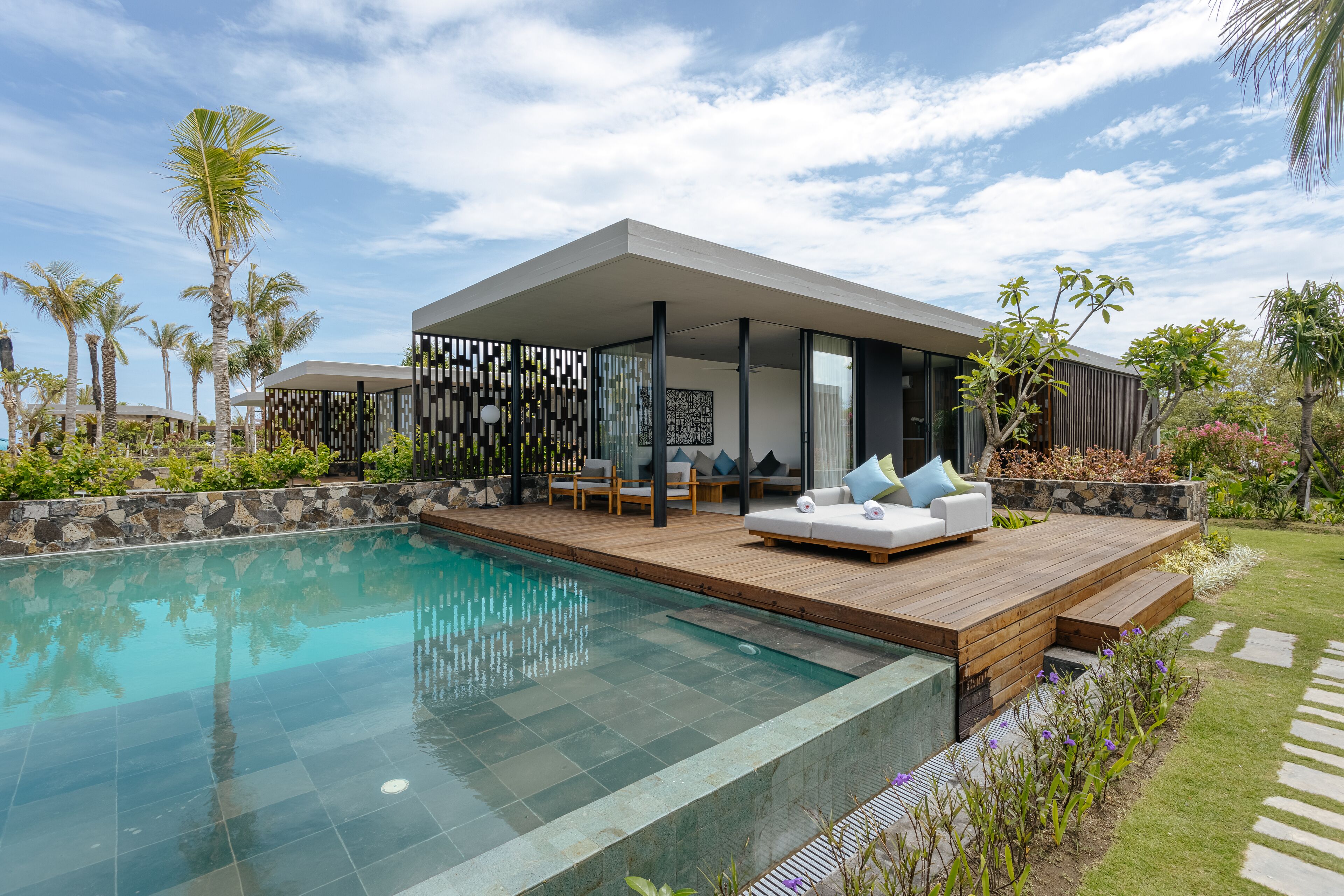 A modern outdoor pool area with a wooden deck, lounge chairs, and a covered seating area.
