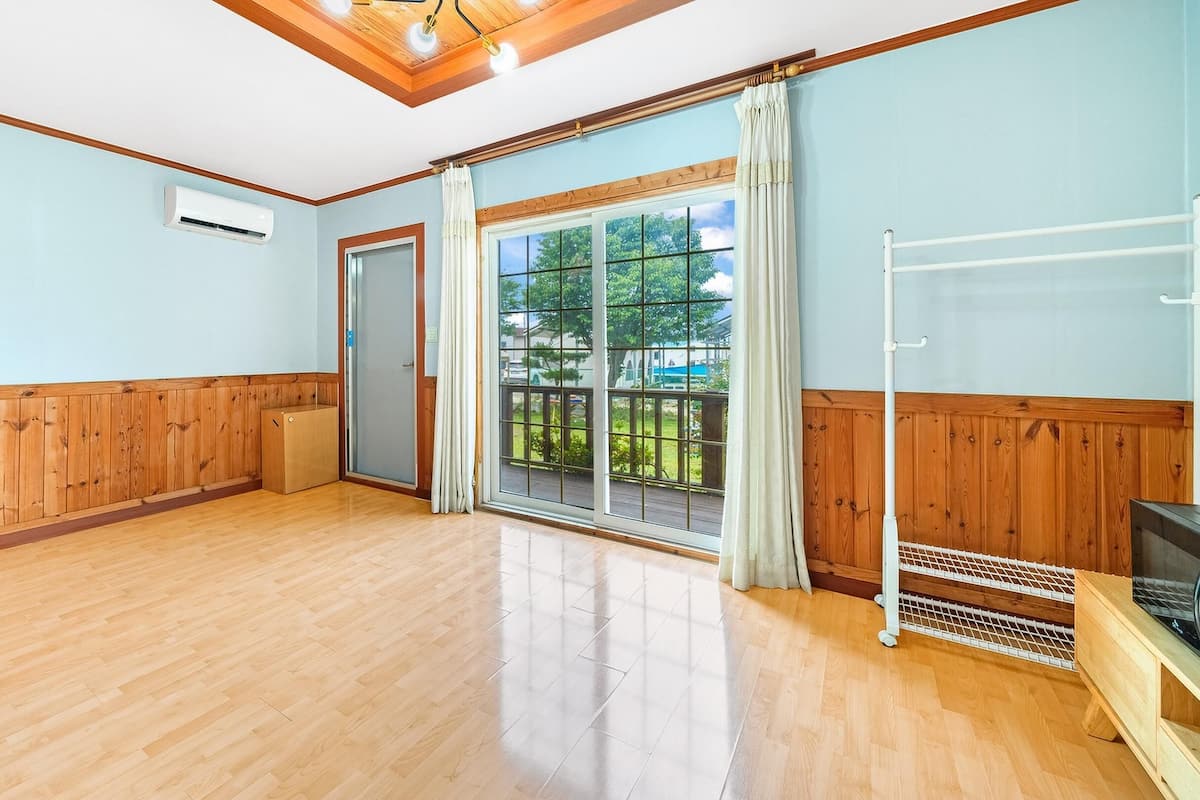 A spacious room with wooden paneling, a large sliding glass door to a balcony, and a built-in TV stand.