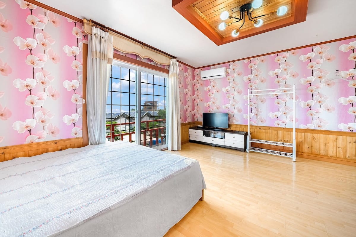 A bedroom with a large bed, a TV, and a balcony with a view.