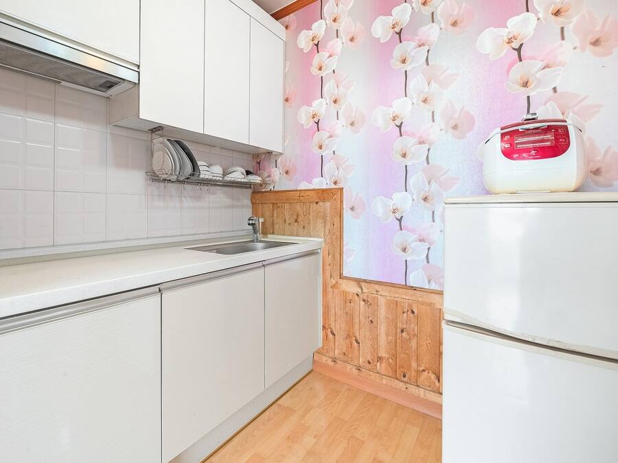 Una cocina con armarios blancos, un lavamanos y un refrigerador blanco.