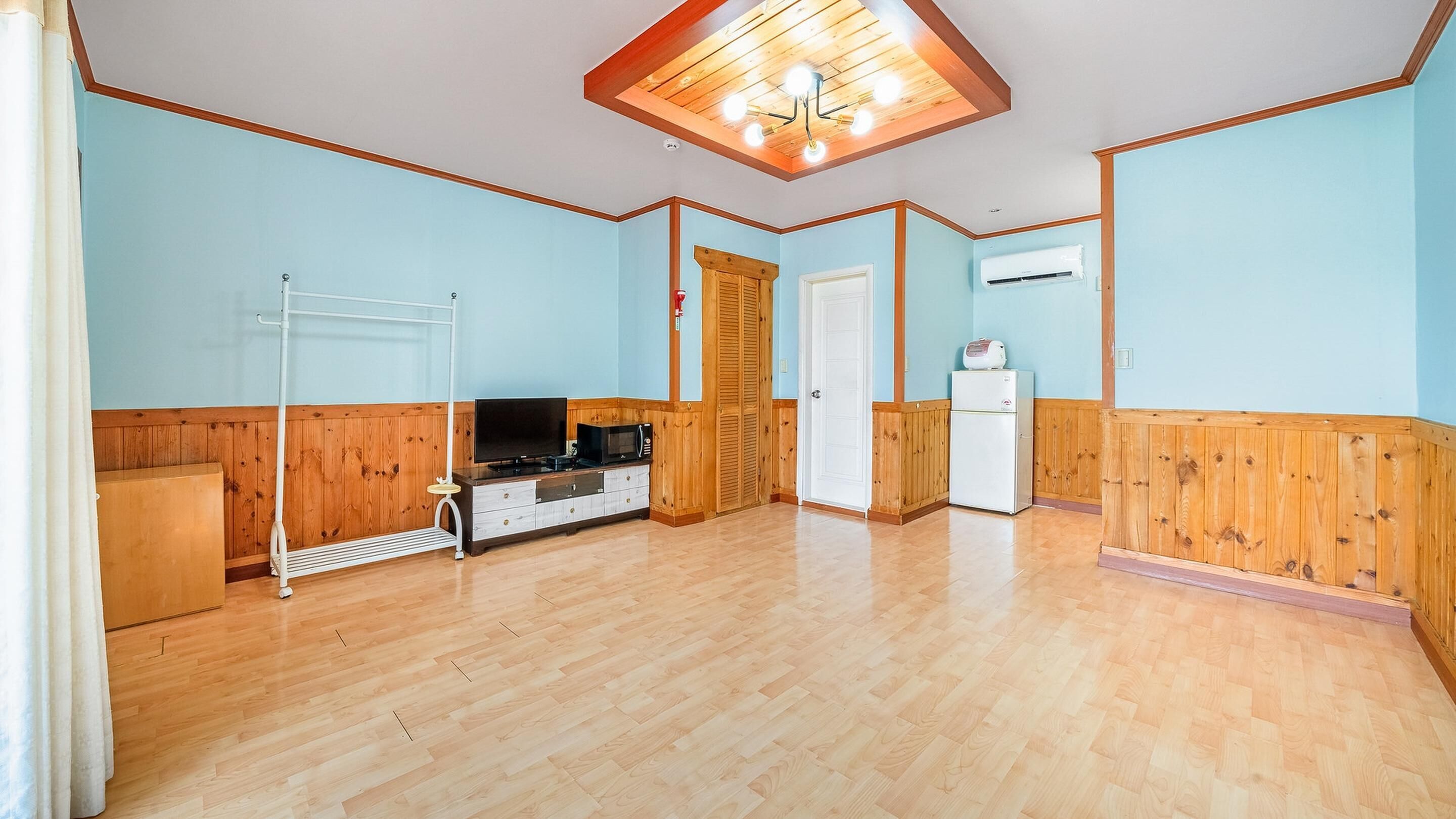 Una habitación con paneles de madera, ventilador de techo, televisor de pantalla plana, microondas, refrigerador y mueble de madera.