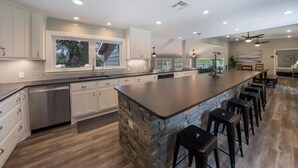 A spacious kitchen with white cabinets, a large island with stools, and a dishwasher. - NB Lakefront Getaway*Luxury on Lake Dunlap (New Braunfels)