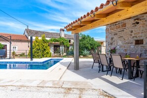 A pool area with a pergola, stone wall, and outdoor seating. - Holiday House Balarini (Gajana)