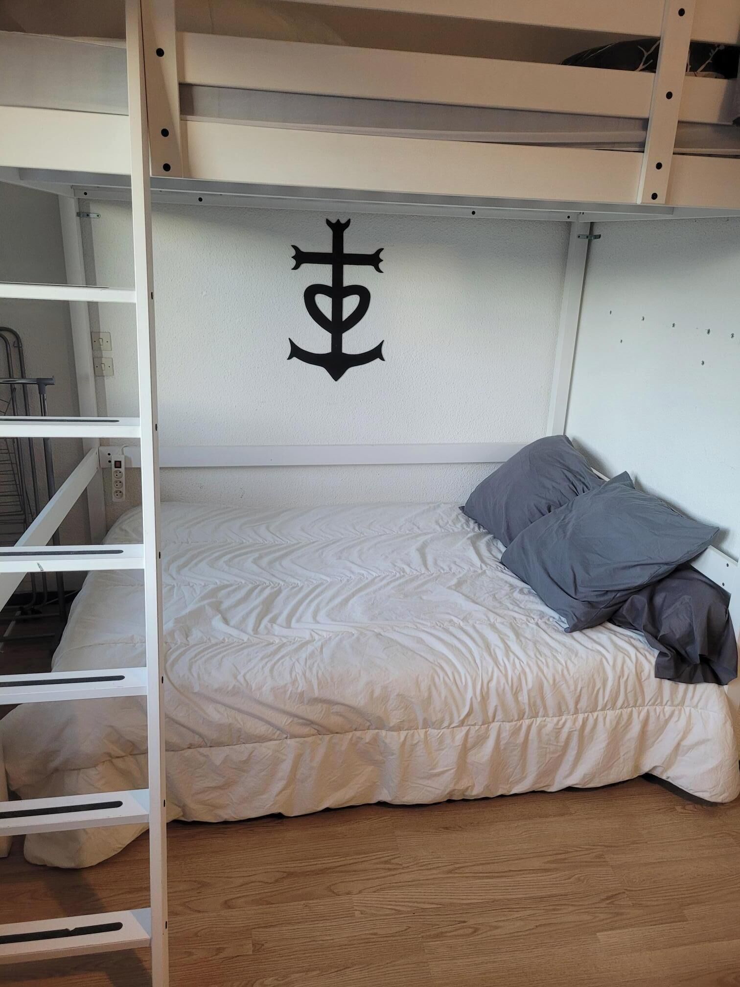 En våningssäng med en vit sänggavel, en säng med ett beige täcke och en grå kudde.