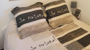 A bed with a world map above it and pillows with 'So Natural' text. - Appartement Rénové Avec une Magnifique vue (Font-Romeu-Odeillo-Via)