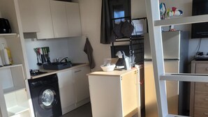 A compact kitchen with a washing machine, a small refrigerator, and a dining area with a table. - Appartement Rénové Avec une Magnifique vue (Font-Romeu-Odeillo-Via)