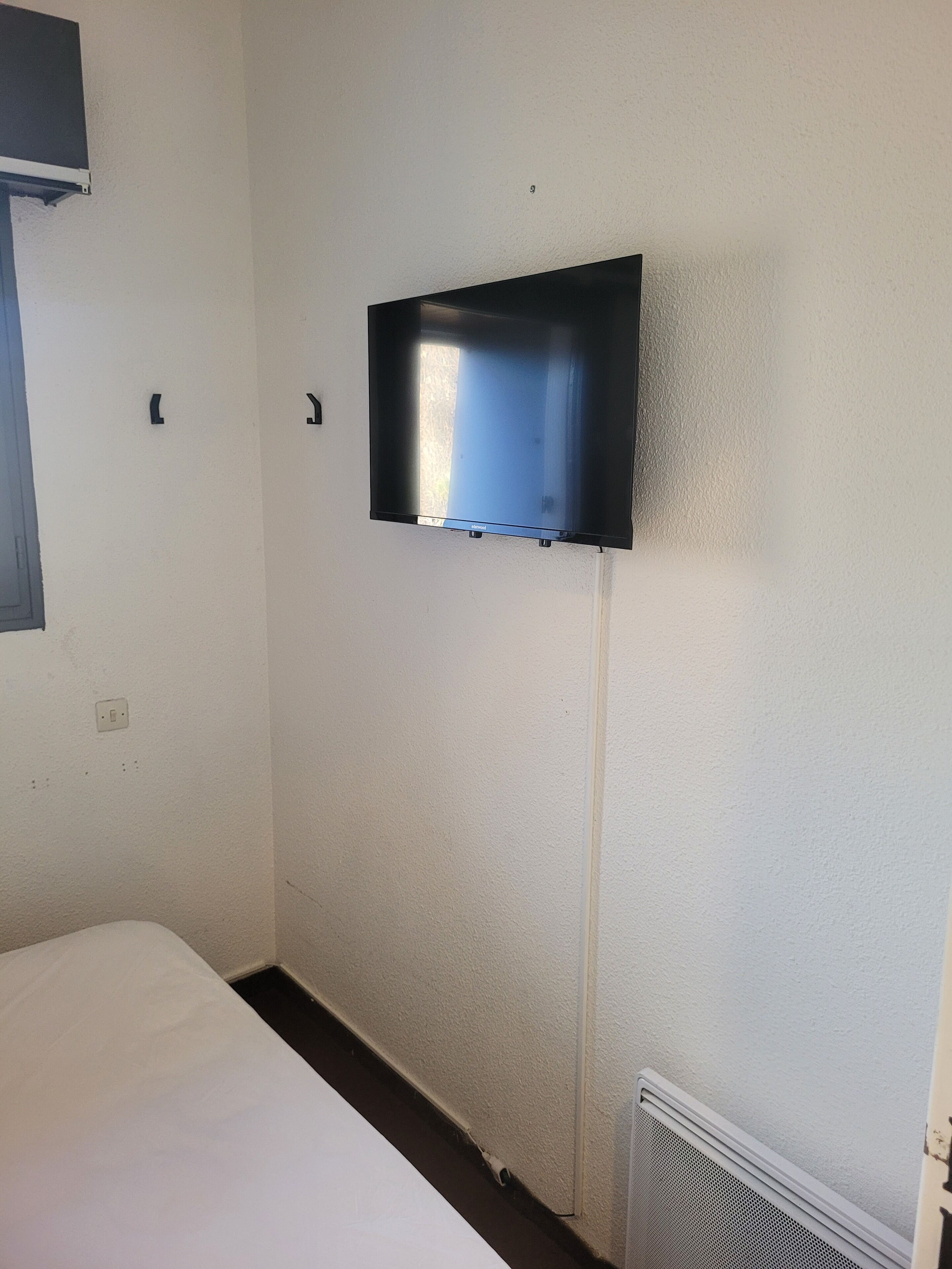 Een kamer met een bed, een tv aan de muur, een stopcontact en een ventilatie rooster.