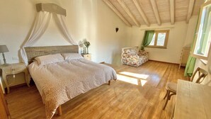Une chambre avec un grand lit, une table de chevet, une chaise et une fenêtre avec des rideaux.