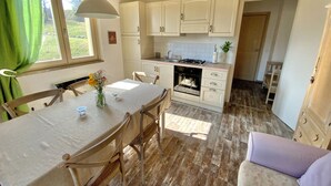 Une cuisine avec des meubles blancs, une cuisinière à gaz et un coin repas comprenant une table et des chaises.