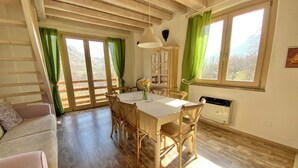 Un coin repas avec des meubles en bois, une table et des chaises. On y trouve une fenêtre avec des rideaux, un radiateur et un luminaire fixé au mur.