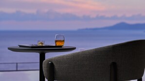 Une table sur laquelle se trouvent un verre contenant un liquide ambré et une petite assiette, le tout mis en valeur par un paysage pittoresque comprenant des montagnes et une étendue d’eau.