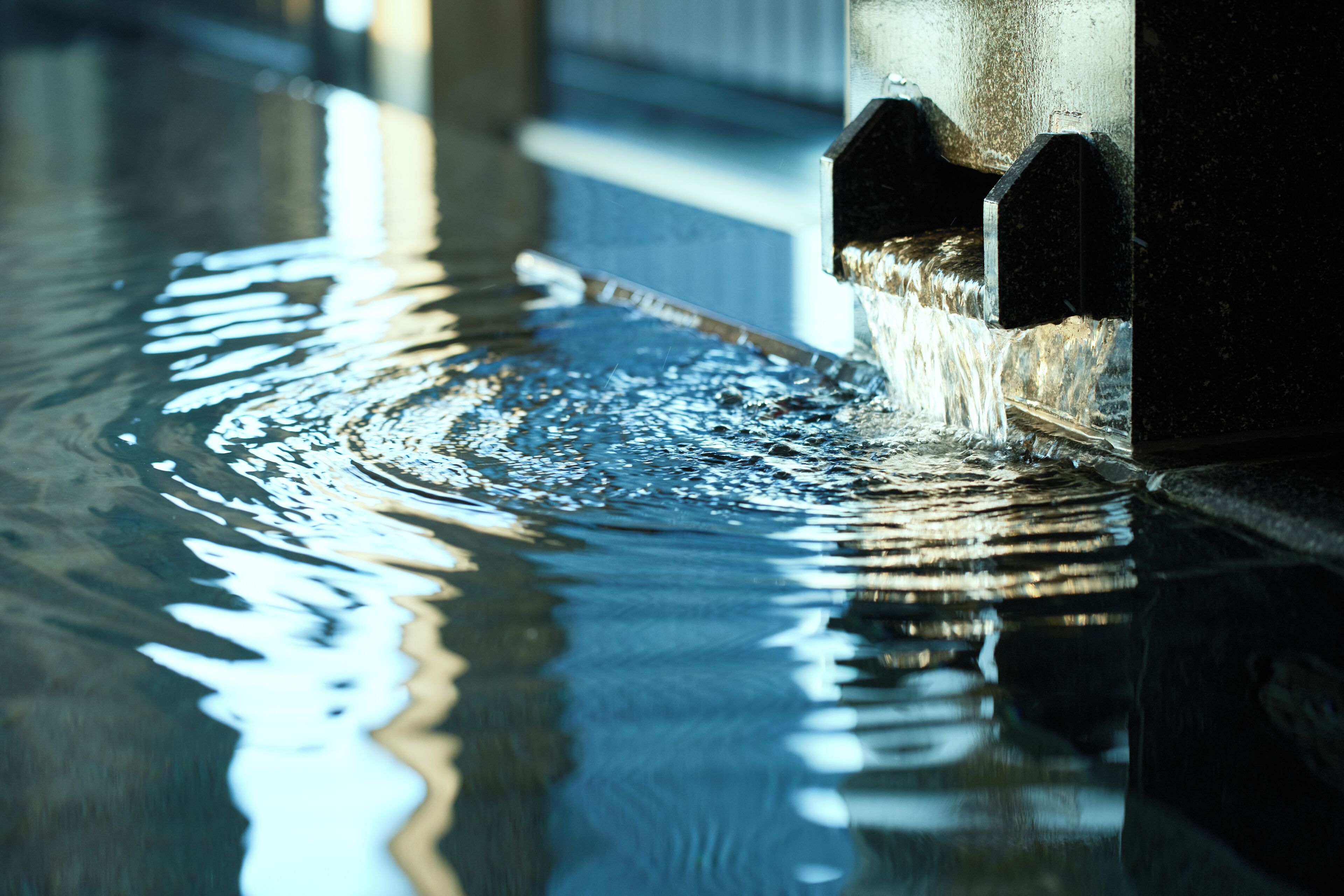 Primer plano de agua brotando de un grifo, creando ondas en una superficie reflectante.