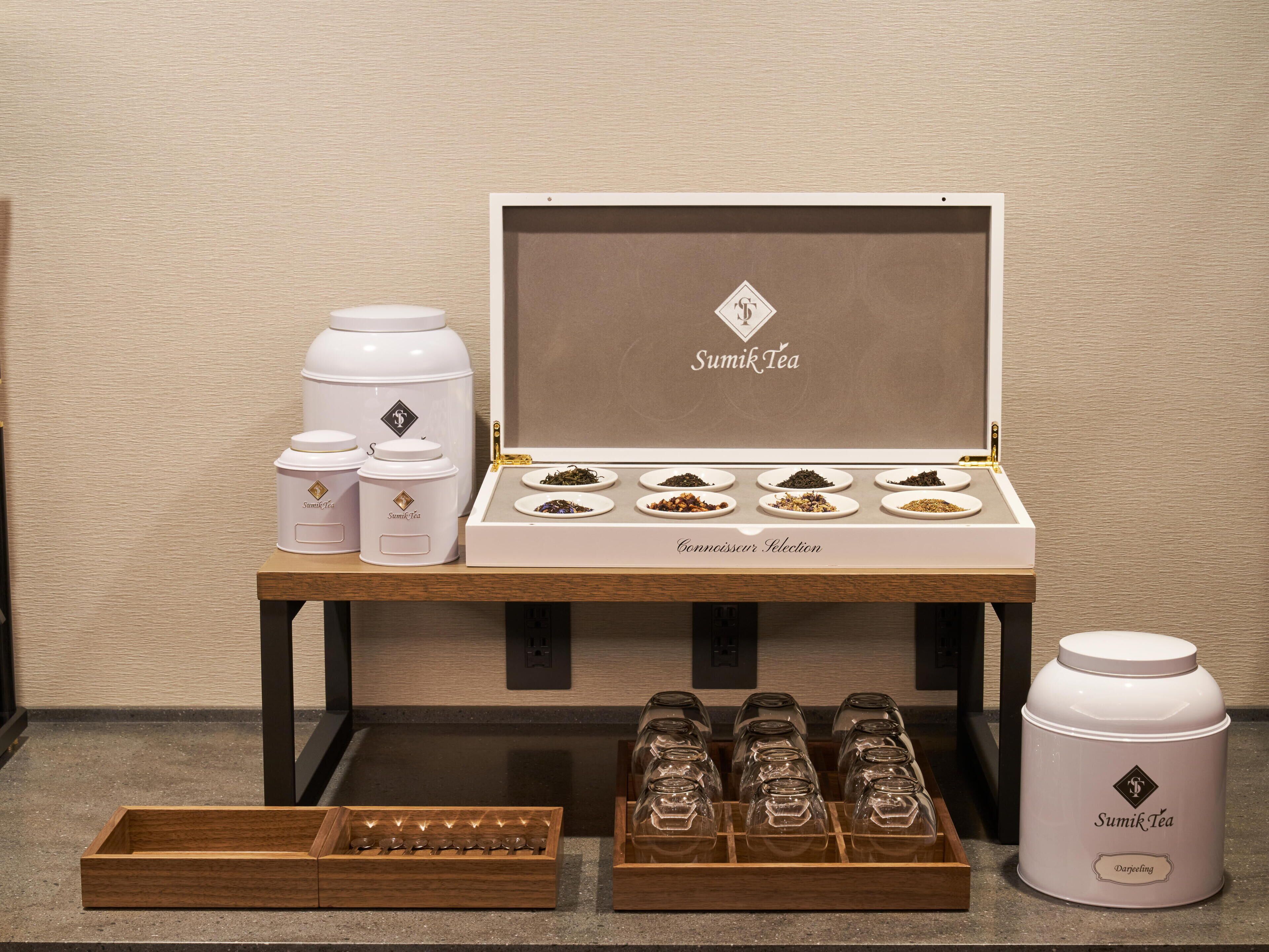 Una presentació de tè amb diferents recipients i pots, incloent una caixa de marca Sumik Tea i alguns pots.