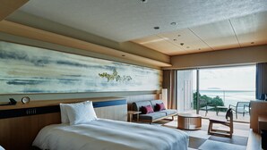 A modern hotel room with a large bed, a sofa, a small table, and a view of the sea. - Atami Izusan KARAKU（ORIX HOTELS & RESORTS） (Atami)