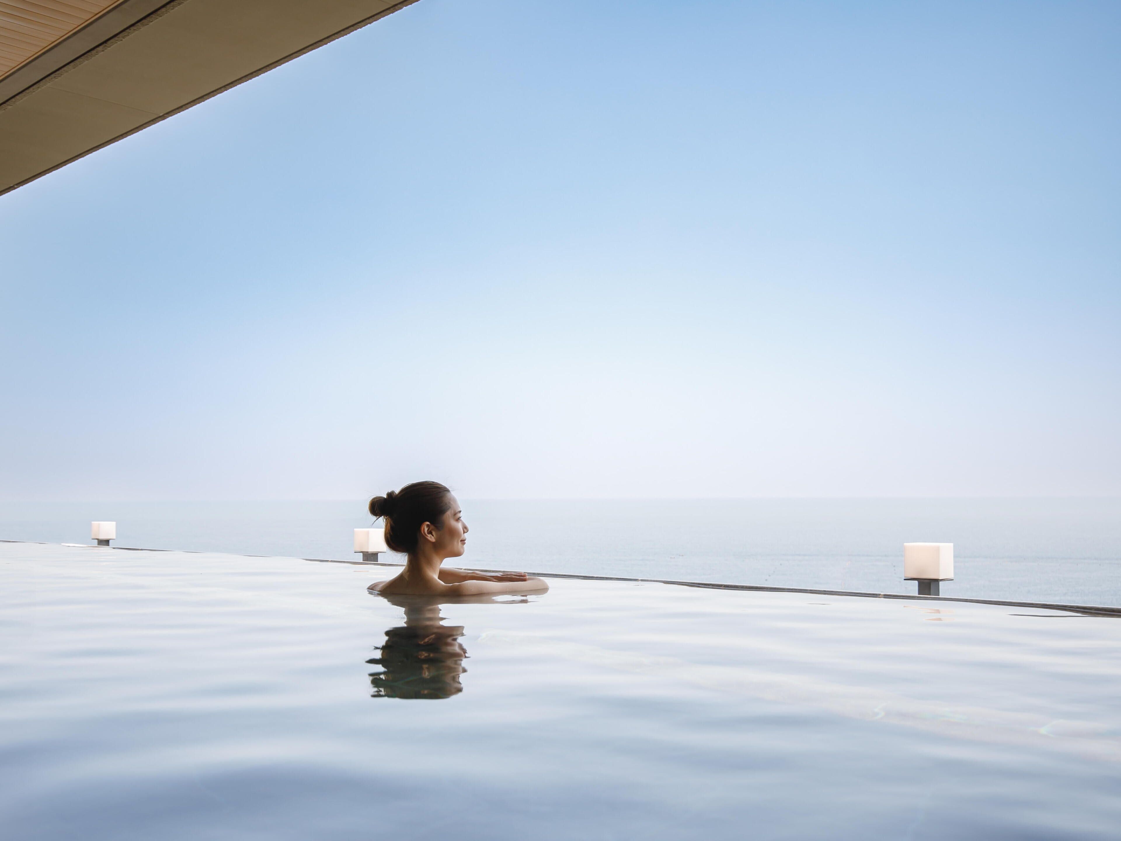 Una persona en una piscina infinita transparente con vista al mar.