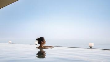 Una persona en una piscina infinita transparente con vista al mar.