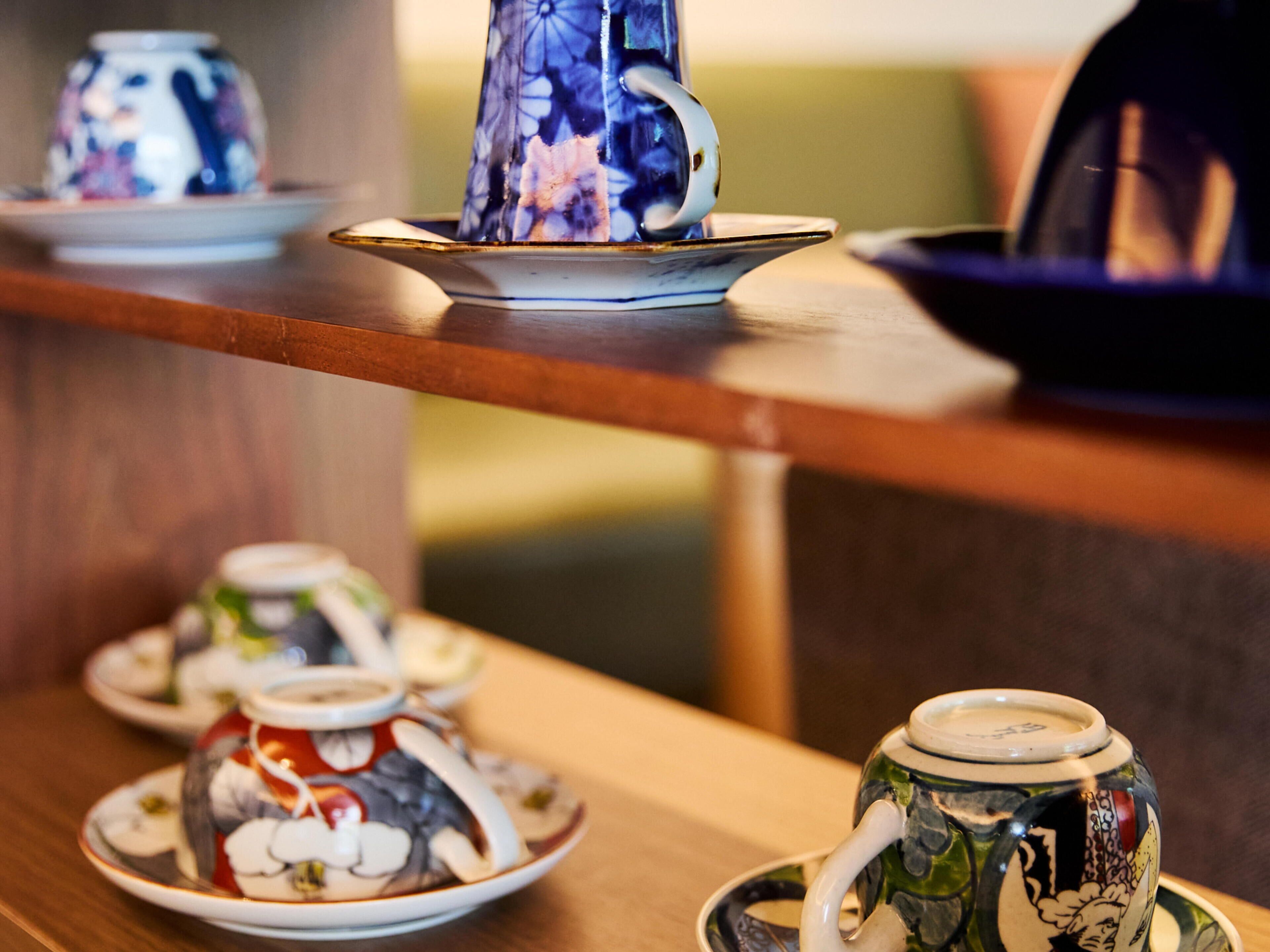 A table with various teapots and cups, some with floral designs, arranged on a wooden surface.