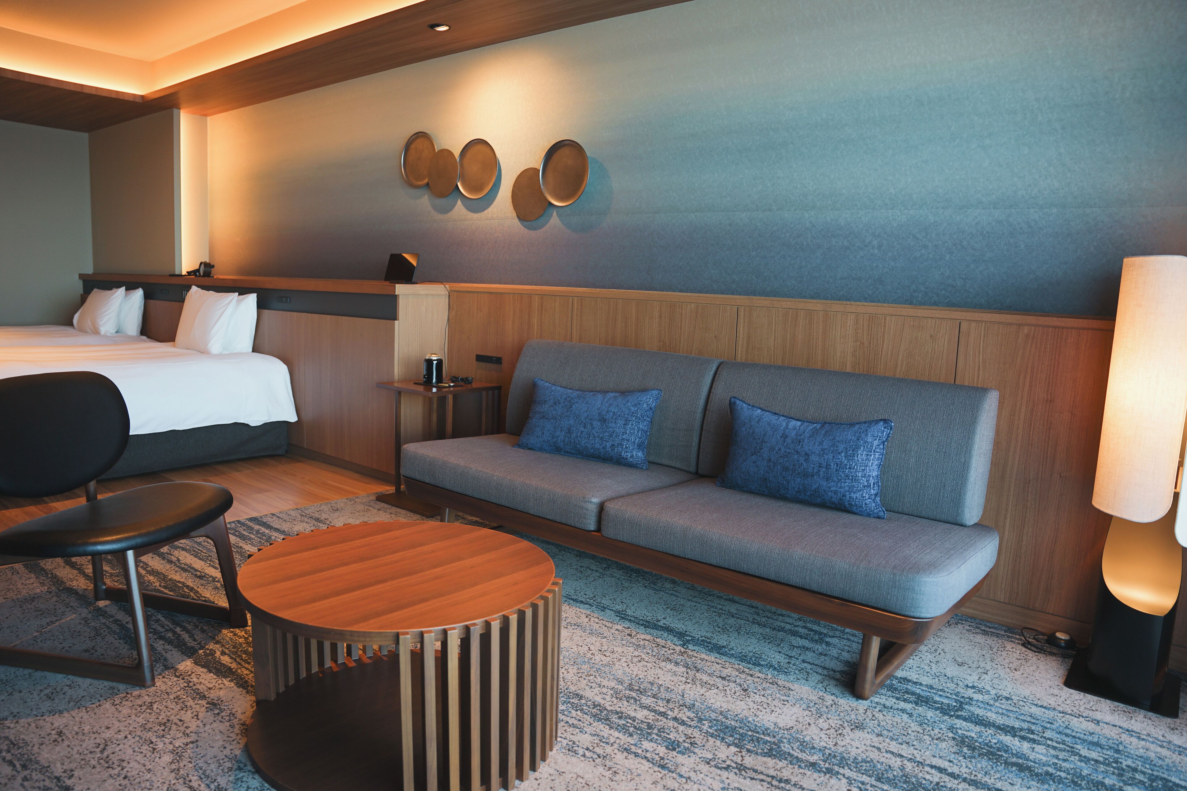 A hotel room with a bed, a sofa, a coffee table, and a lamp.
