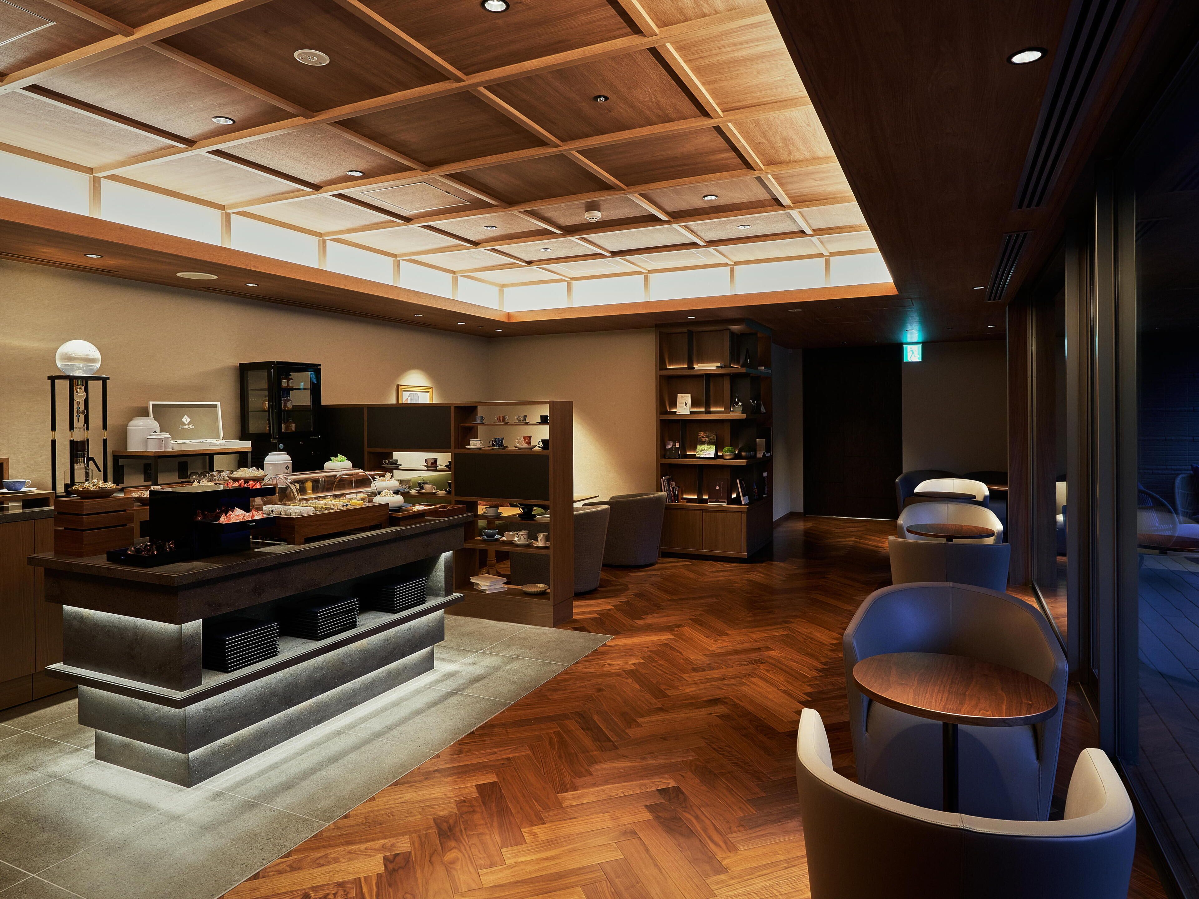 A modern interior with a wooden ceiling, a buffet area, seating, and a large window.