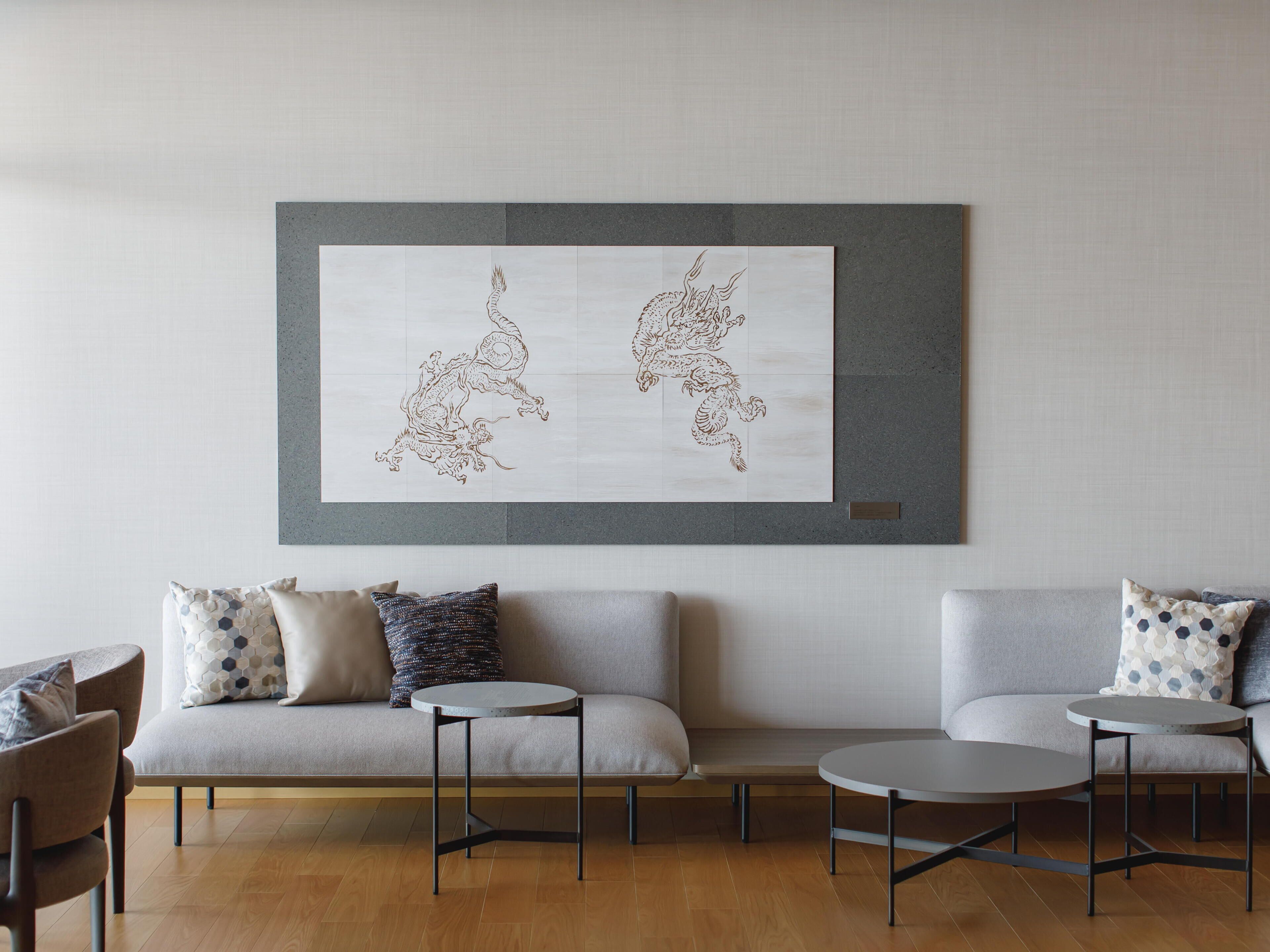 A modern living room with a grey sofa, two round tables, and a large framed artwork of two dragons on the wall.