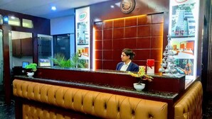 A reception area with a brown leather bench, a clock, and a poster with the WP logo. - West Park Inn (Dhaka)