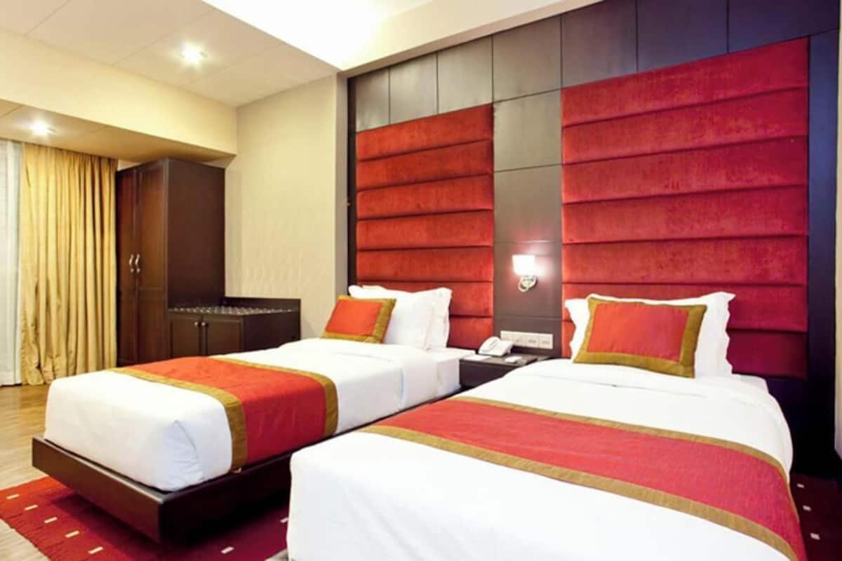 Quarto de hotel com duas camas, um guarda-roupa e uma cabeceira grande vermelha.