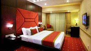 A hotel room with a large bed, a nightstand, a desk, and a television. - West Park Inn (Dhaka)