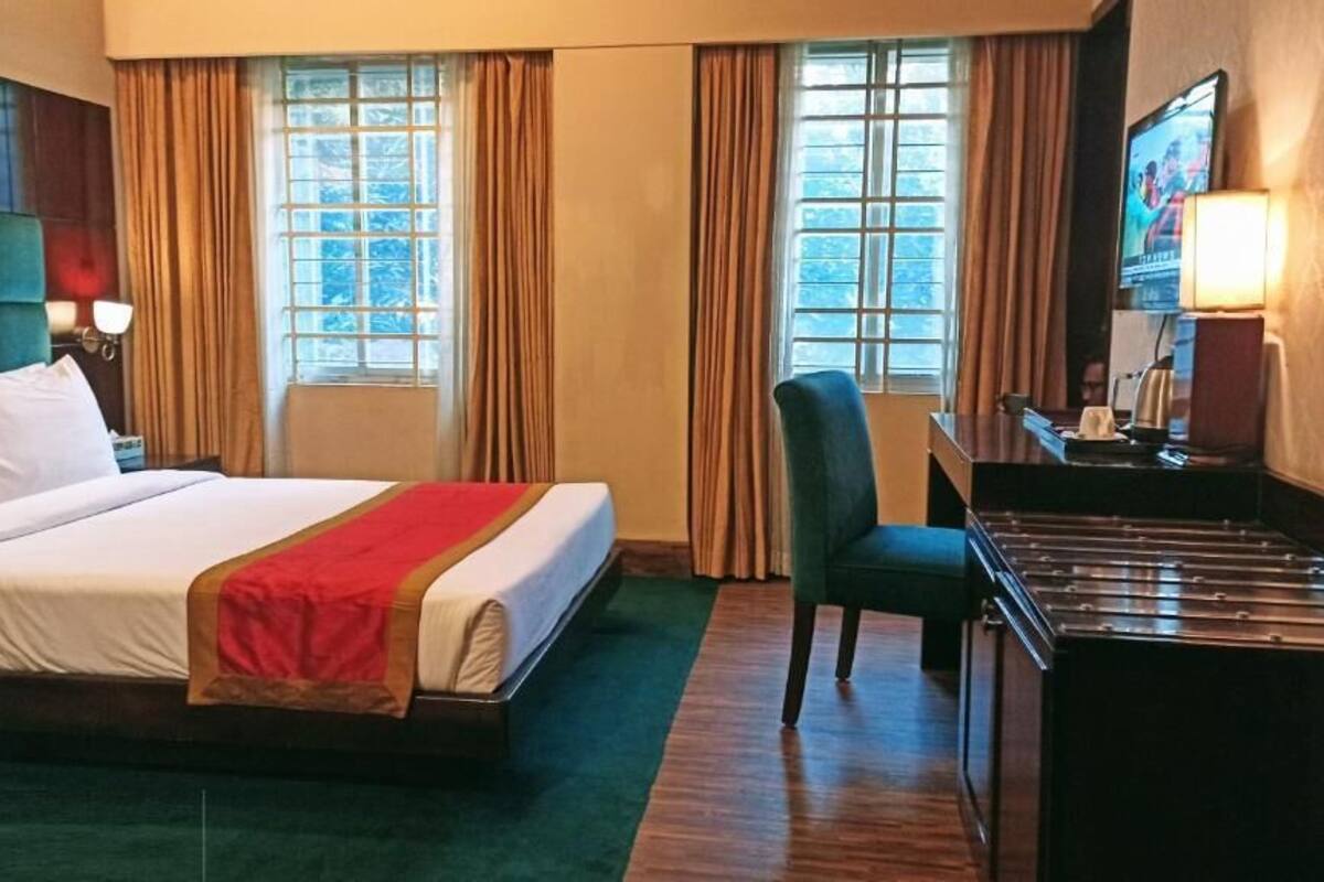Quarto de hotel com cama, escrivaninha, cadeira e televisão.