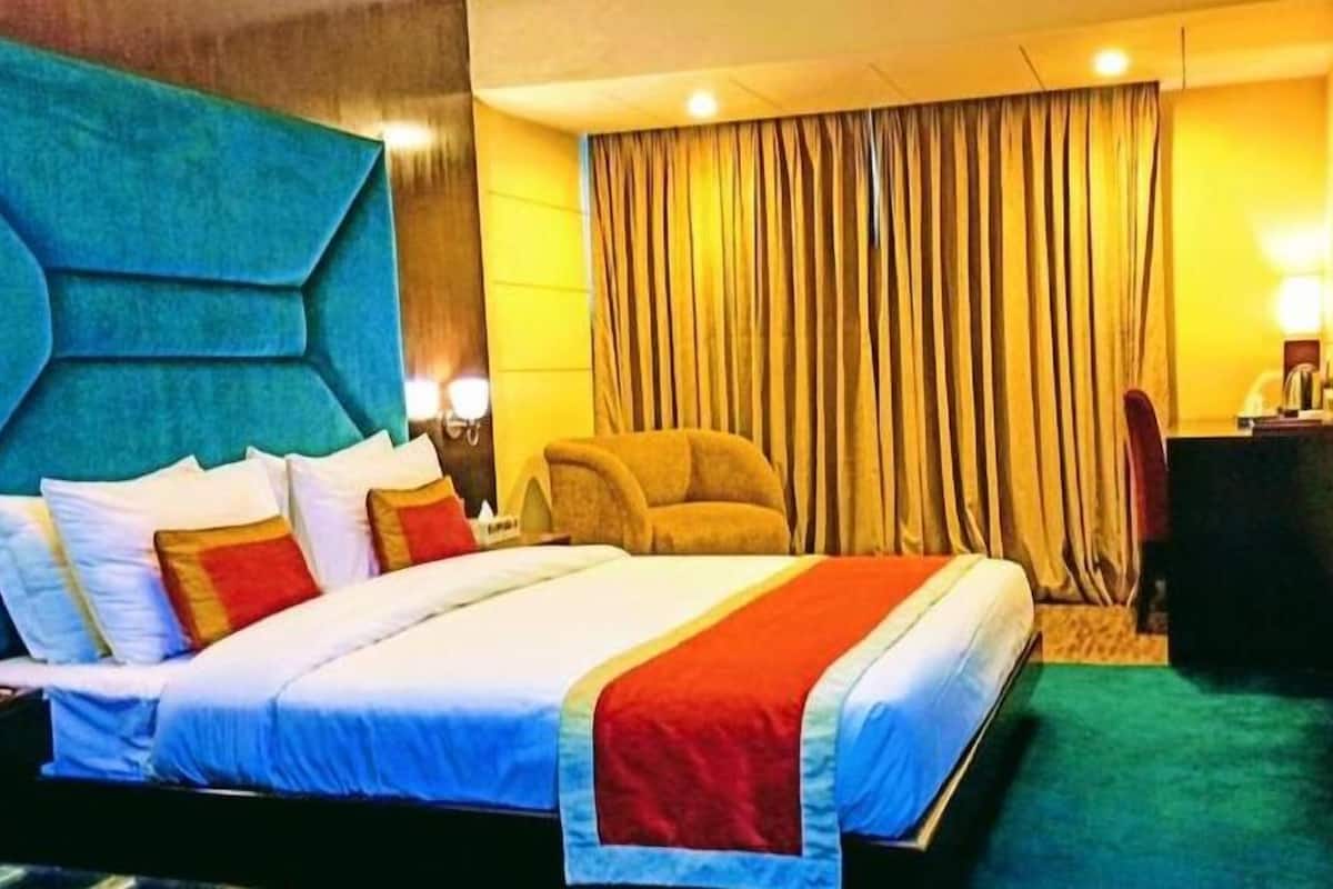 Quarto de hotel com uma cama grande, uma cadeira, uma escrivaninha e cortina.
