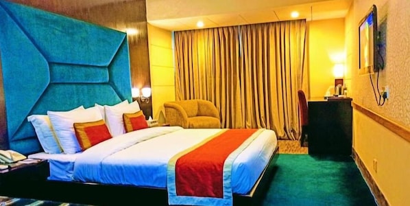 A hotel room with a large bed, a chair, a desk, and a curtain. - West Park Inn (Dhaka)