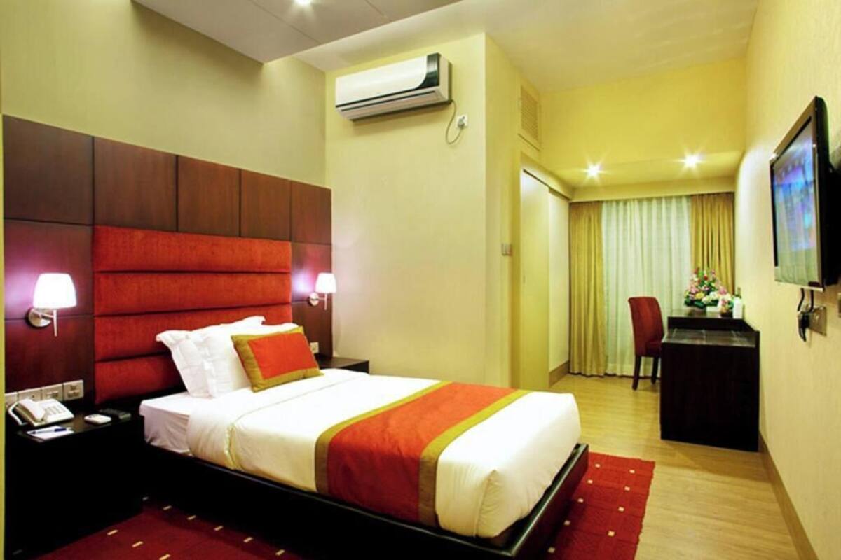 Quarto de hotel com uma cama grande, uma escrivaninha, uma cadeira, ar condicionado e uma televisão.
