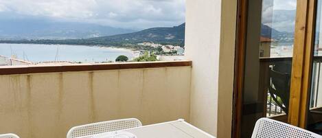 A balcony with a table set for two, overlooking a coastal landscape with mountains in the distance.