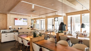 A modern restaurant with wooden interiors, large windows, and a variety of seating arrangements. - Nordic Hostel (Lantsch-Lenz)