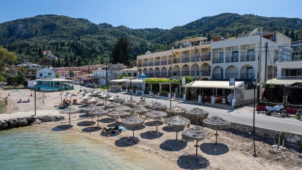 A coastal town with a beach, umbrellas, and buildings. - Riviera Seaside Hotel by Estia (Corfu)