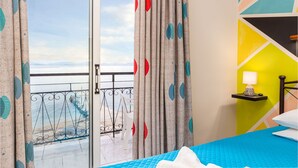 A hotel room with a bed, a nightstand, a lamp, and a view of the sea through a balcony door. - Riviera Seaside Hotel by Estia (Corfu)