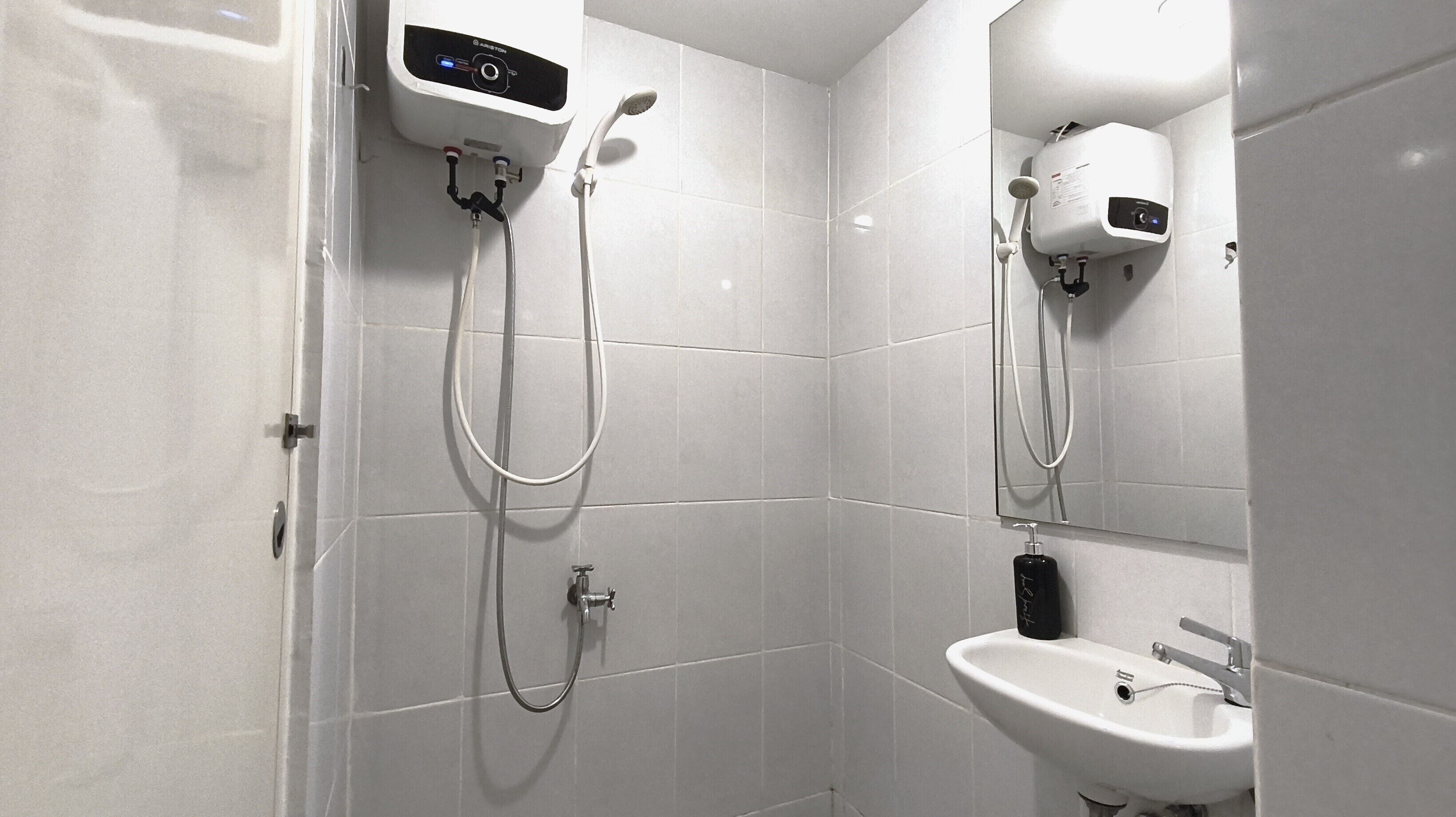 A bathroom with white tiled walls, a white sink, and two shower units with control panels.