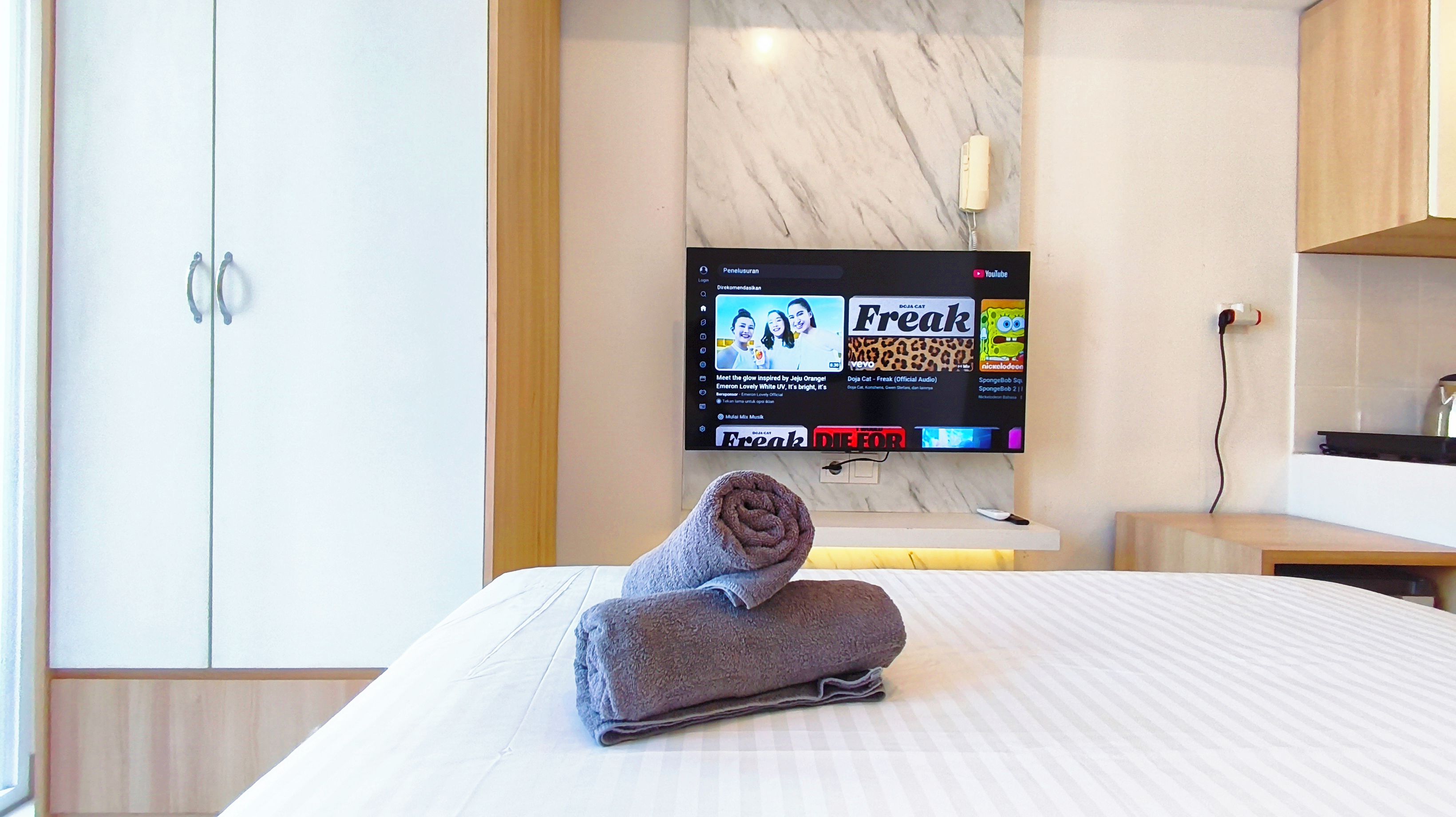 A hotel room with a bed, a TV on the wall, and a towel on the bed.