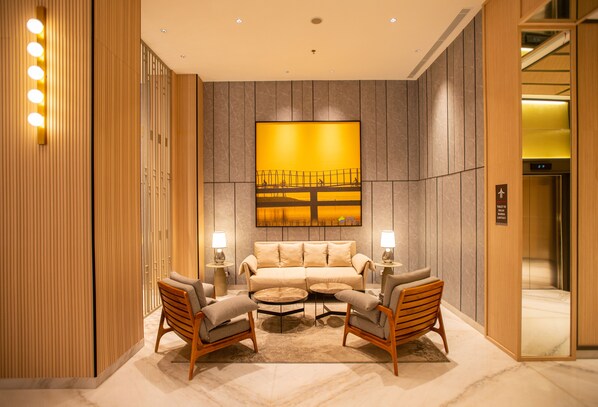 A modern lobby with a sofa set, two armchairs, a coffee table, and a large abstract painting on the wall.