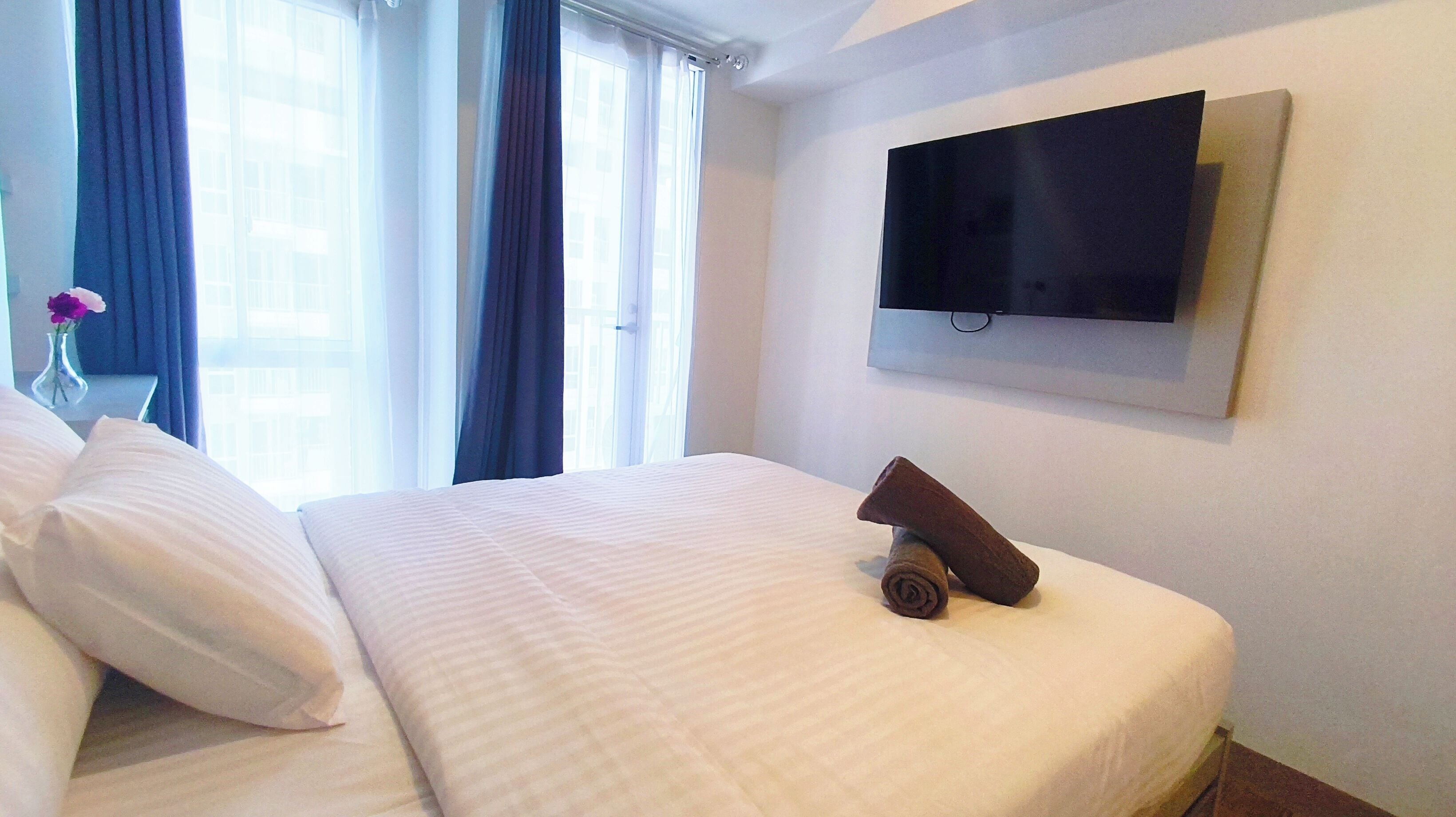 A hotel room with a bed, a TV mounted on the wall, and a window with curtains.