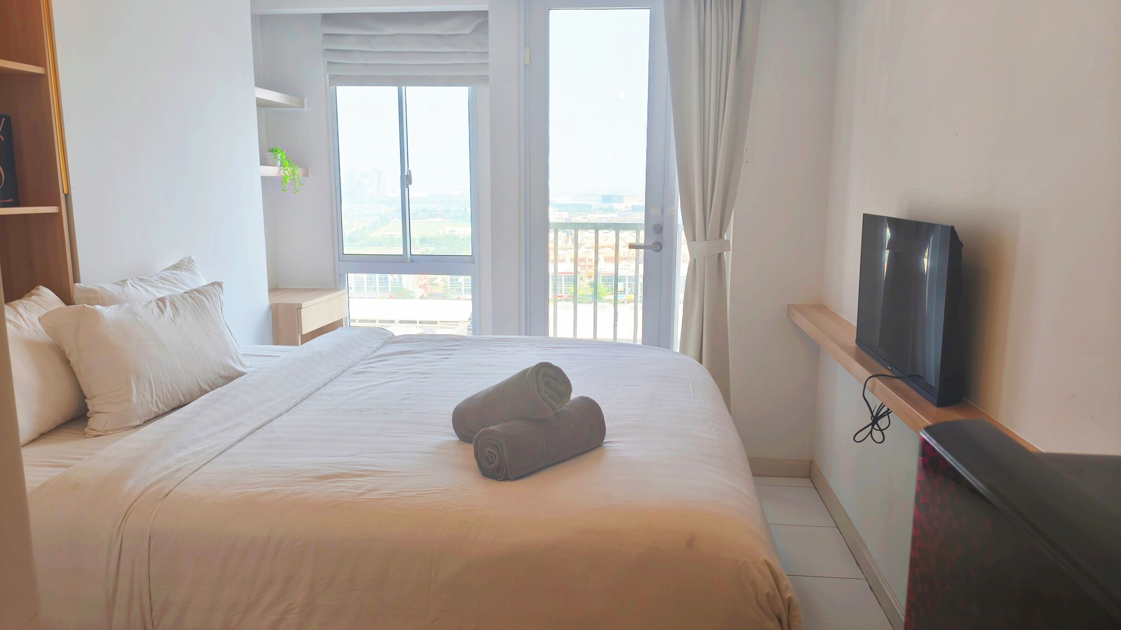 Una habitación de hotel con cama, televisión, balcón con cortinas y vistas a la ciudad.