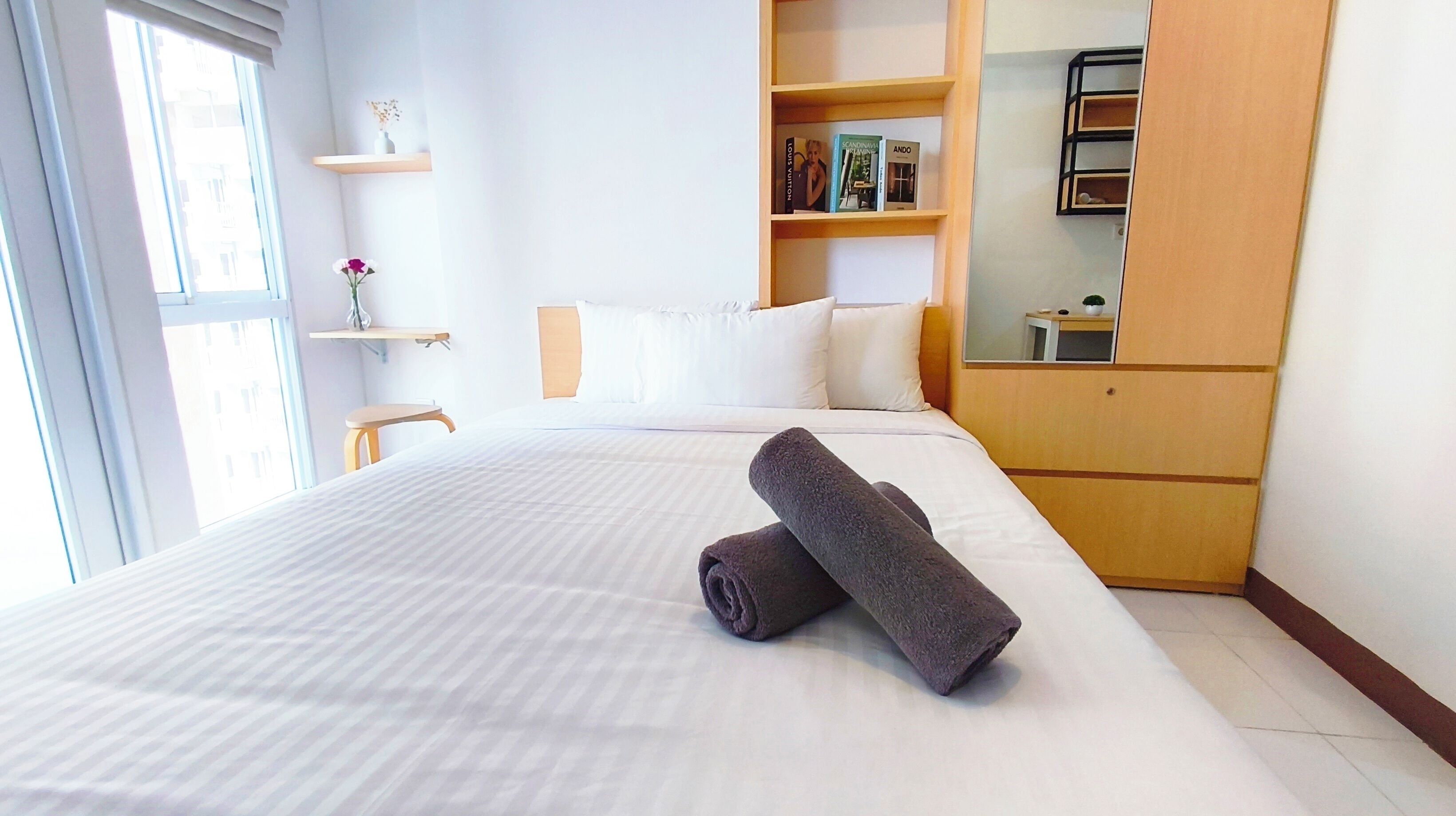 A hotel room with a large bed, a wooden wardrobe, a small table, and a window.